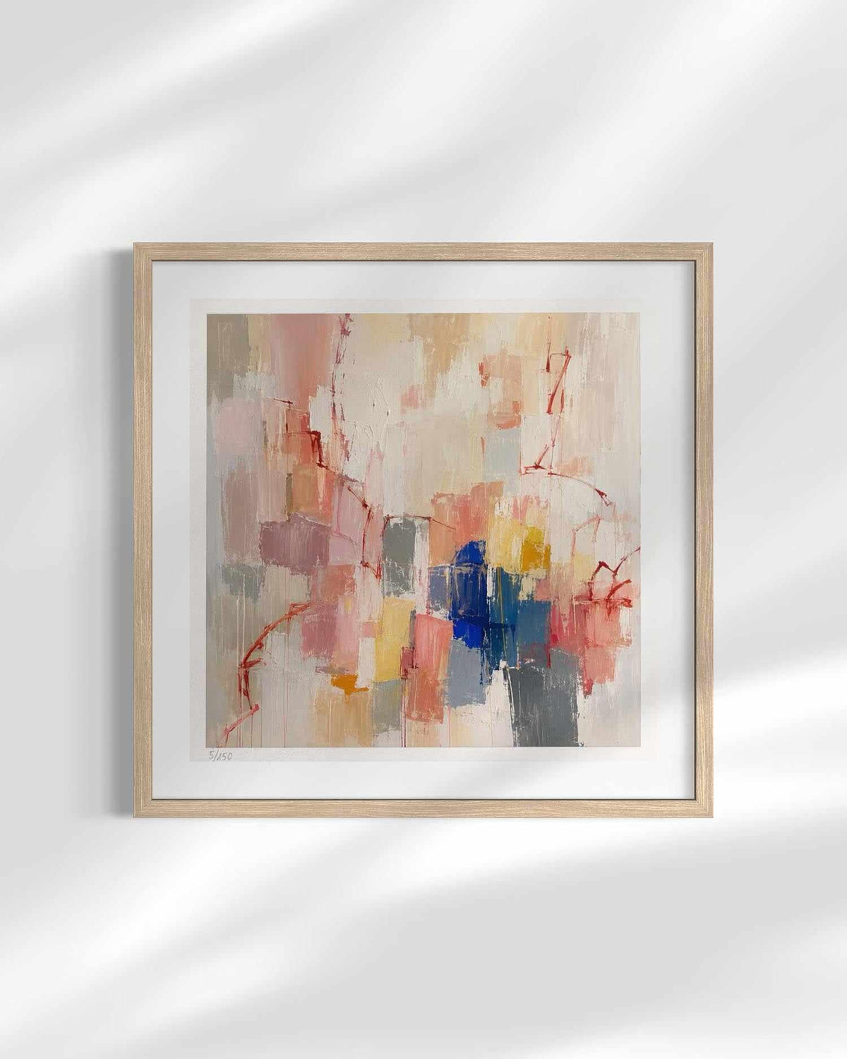 A framed abstract art print featuring a mix of soft beige, pink, red, blue, and gray brushstrokes, housed in a light natural wood frame with a white mat, displayed against a white wall with soft diagonal shadows.