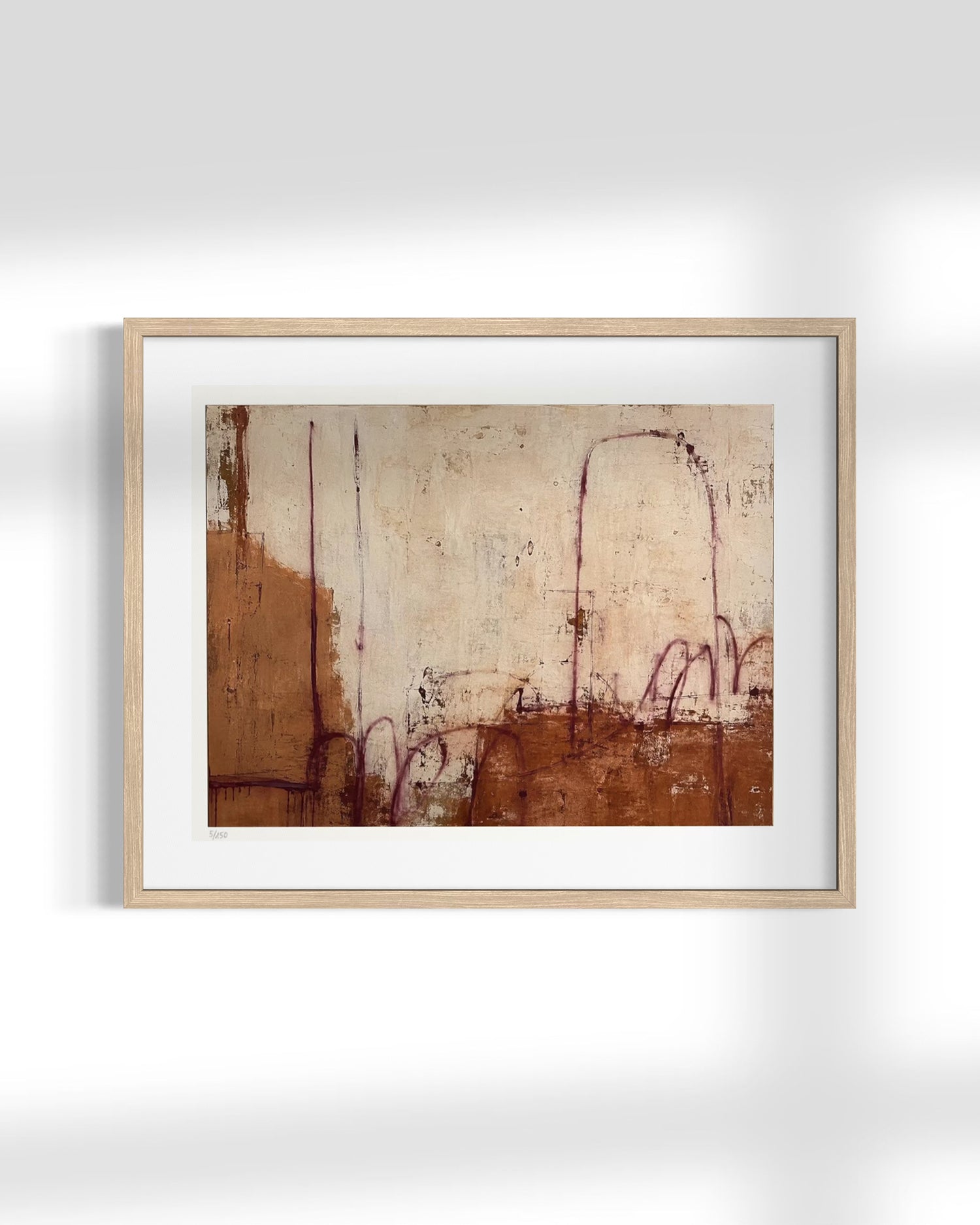 A framed abstract art print featuring earthy brown and beige tones with delicate reddish-purple sketch-like lines, presented in a light natural wood frame with a white mat against a clean white wall.