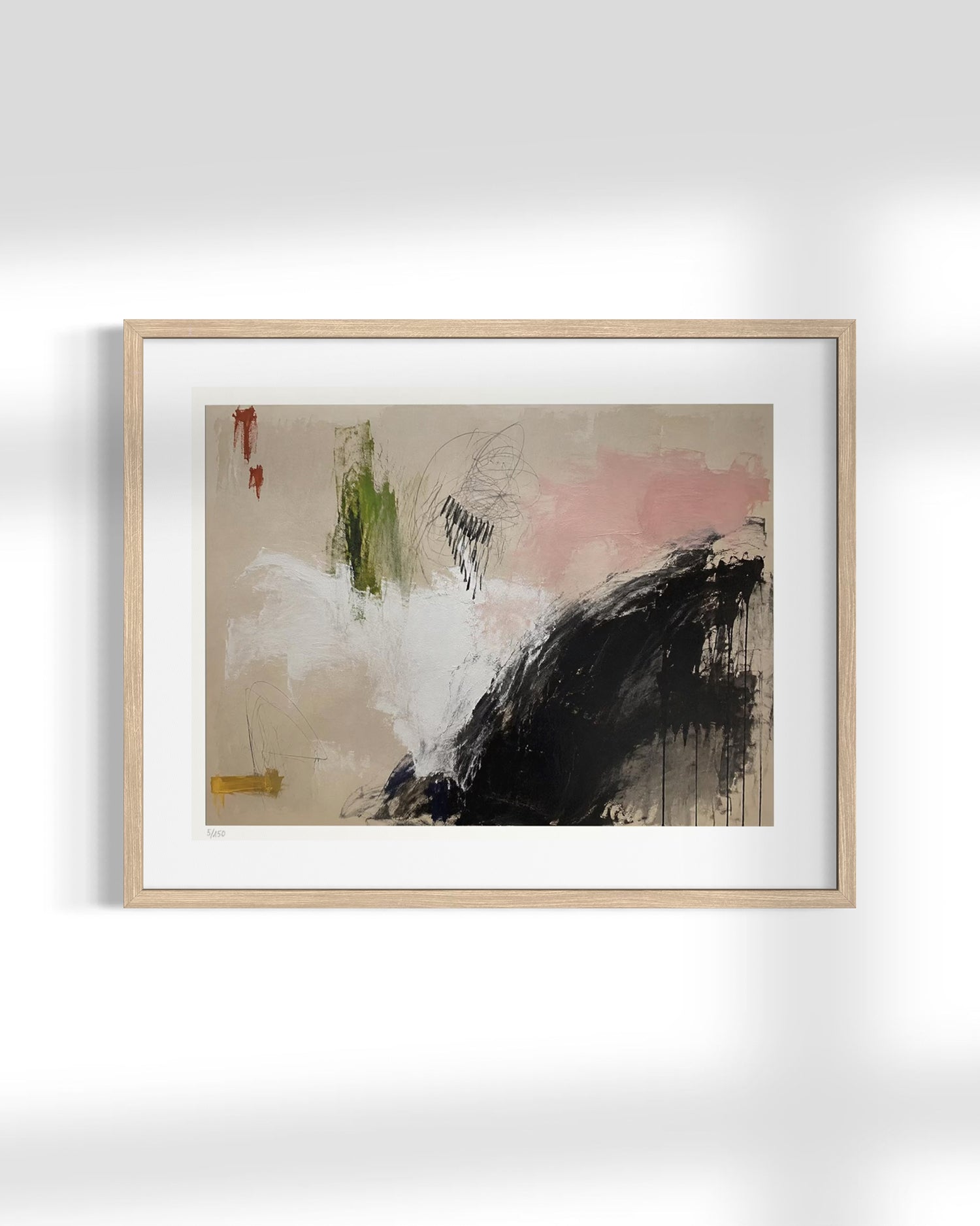 A framed abstract art print featuring a modern composition of black, white, pink, beige, green, and red brushstrokes, housed in a light natural wood frame with a white mat, displayed against a white wall with soft shadows.