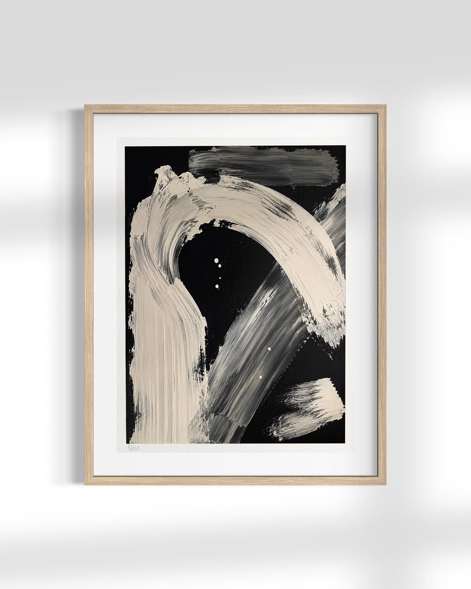 Framed abstract wall art featuring bold beige and gray brushstrokes on a black background, presented in a light wood frame with a white mat against a white wall.