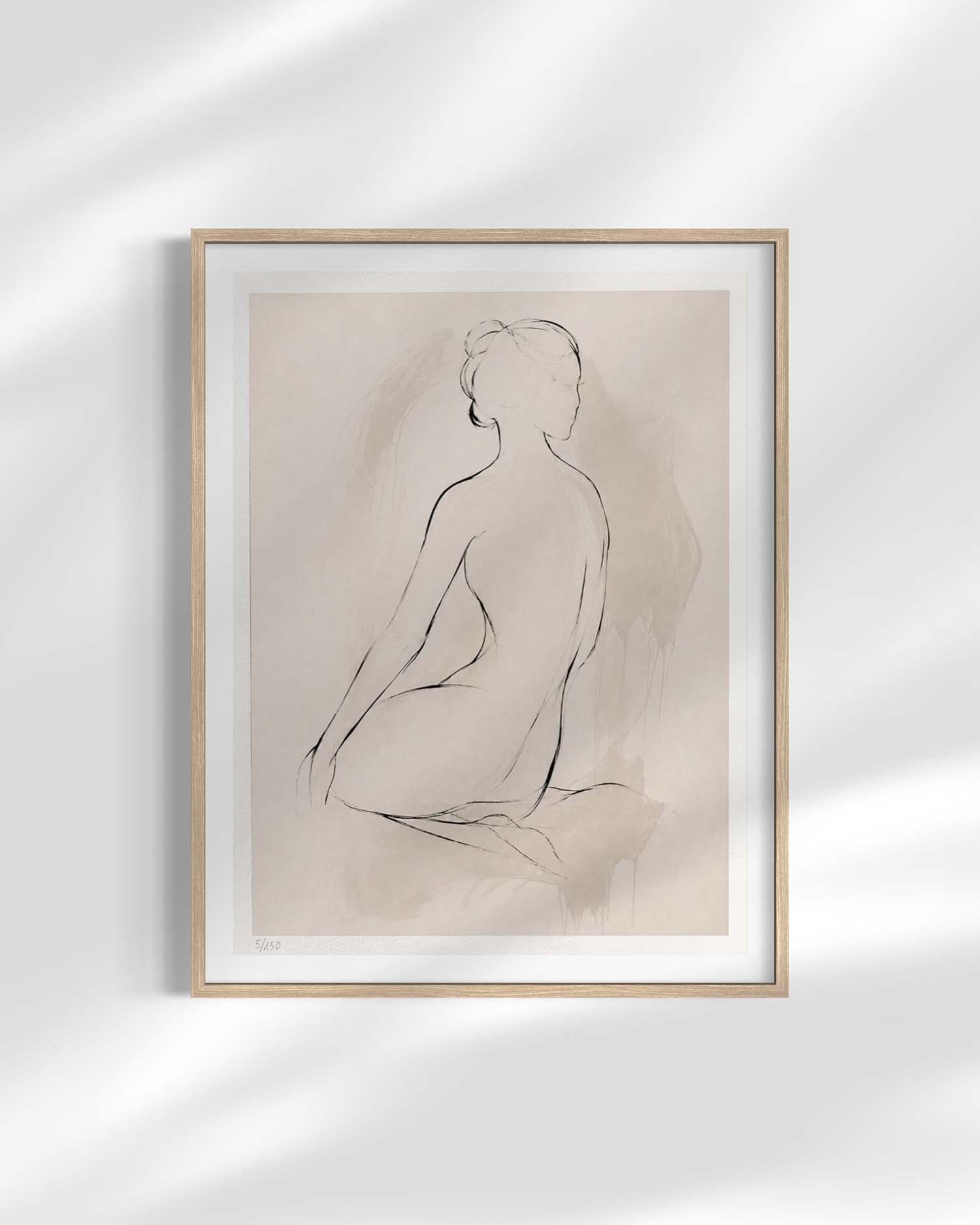 A minimalist framed art print featuring a black line drawing of a seated nude figure on a warm beige background, enclosed in a light wood frame with a white mat, displayed against a white wall with soft shadow overlays.