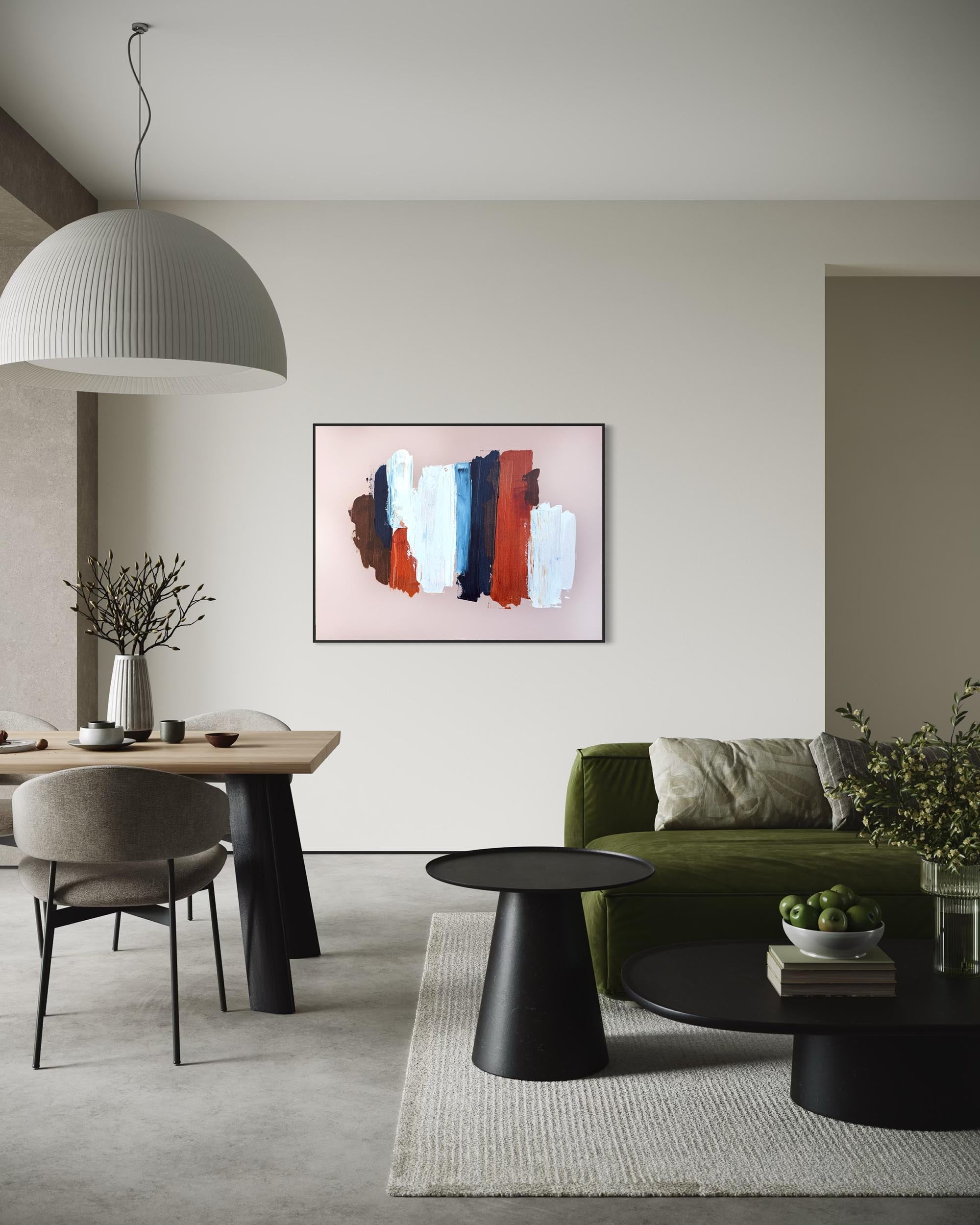 An abstract framed wall art print with vertical brushstrokes in red, blue, white, and brown on a pale pink background, displayed in a modern living room setting above a green sofa.