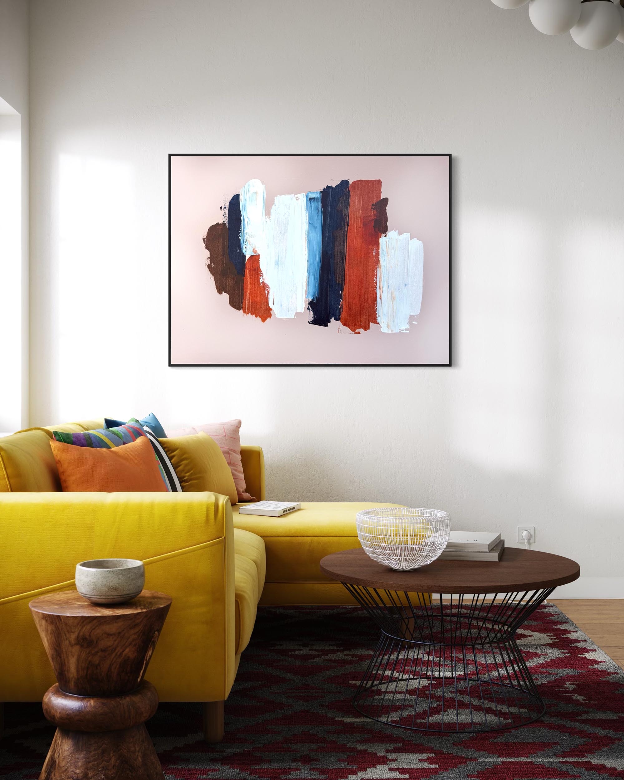 A framed abstract canvas print with vertical brushstrokes in pink, white, blue, brown, and rust red, displayed on a white wall above a yellow sectional sofa in a modern living room setting.