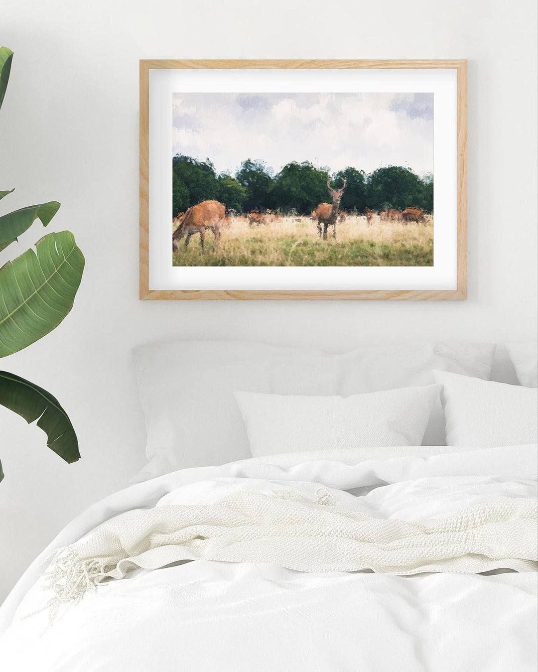 Framed print of deer in a field on a wall above a bed.