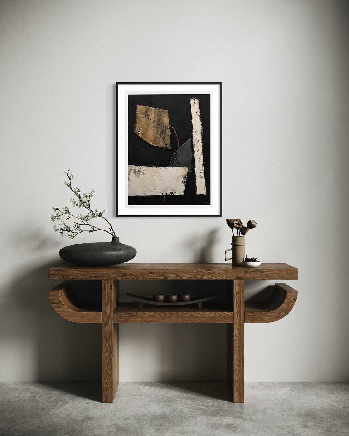 A framed abstract art print with black, beige, and white brushstrokes hangs on a light gray wall above a rustic wooden console table styled with a black ceramic vase and dried branches.