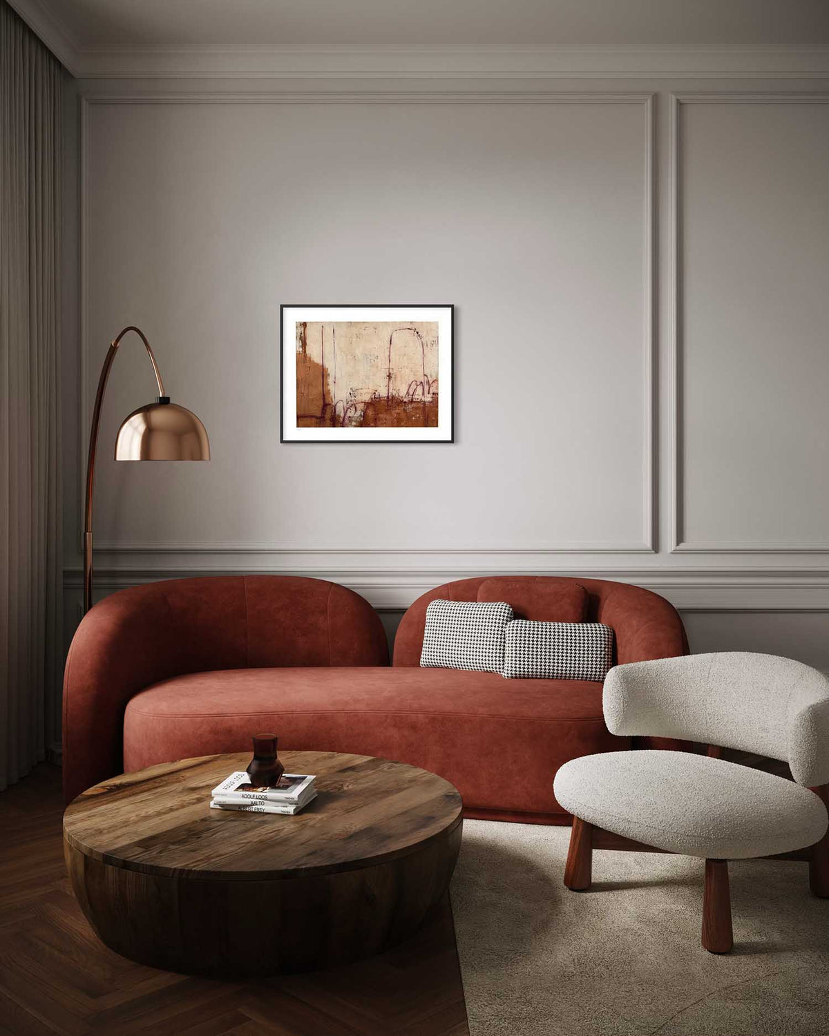 A framed abstract art print with warm earthy tones hangs on a gray paneled wall above a terracotta-colored sofa in a modern living room setting.