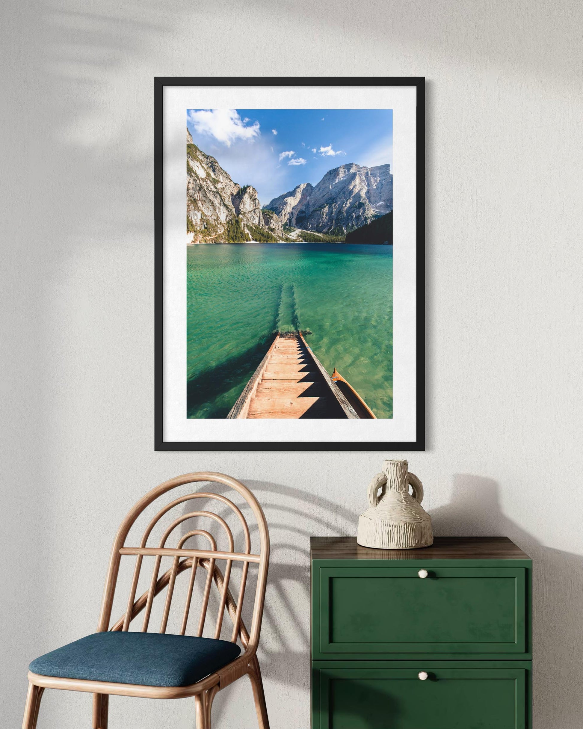 Framed photograph of a mountain lake with a wooden pier, displayed on a wall above a chair and green cabinet.