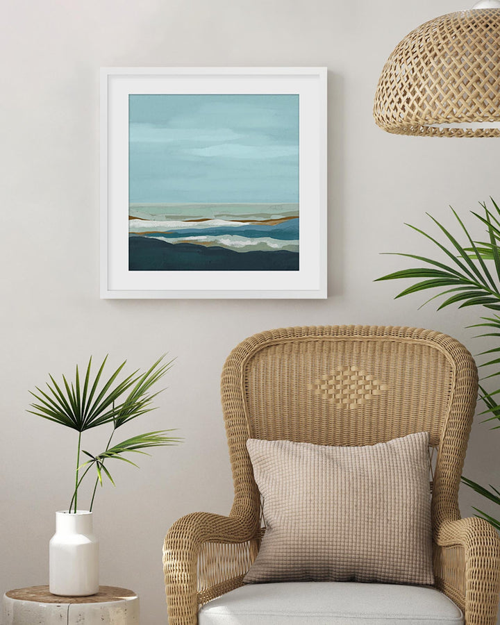 Wicker armchair with a pillow, framed artwork, and plants in a room setting.