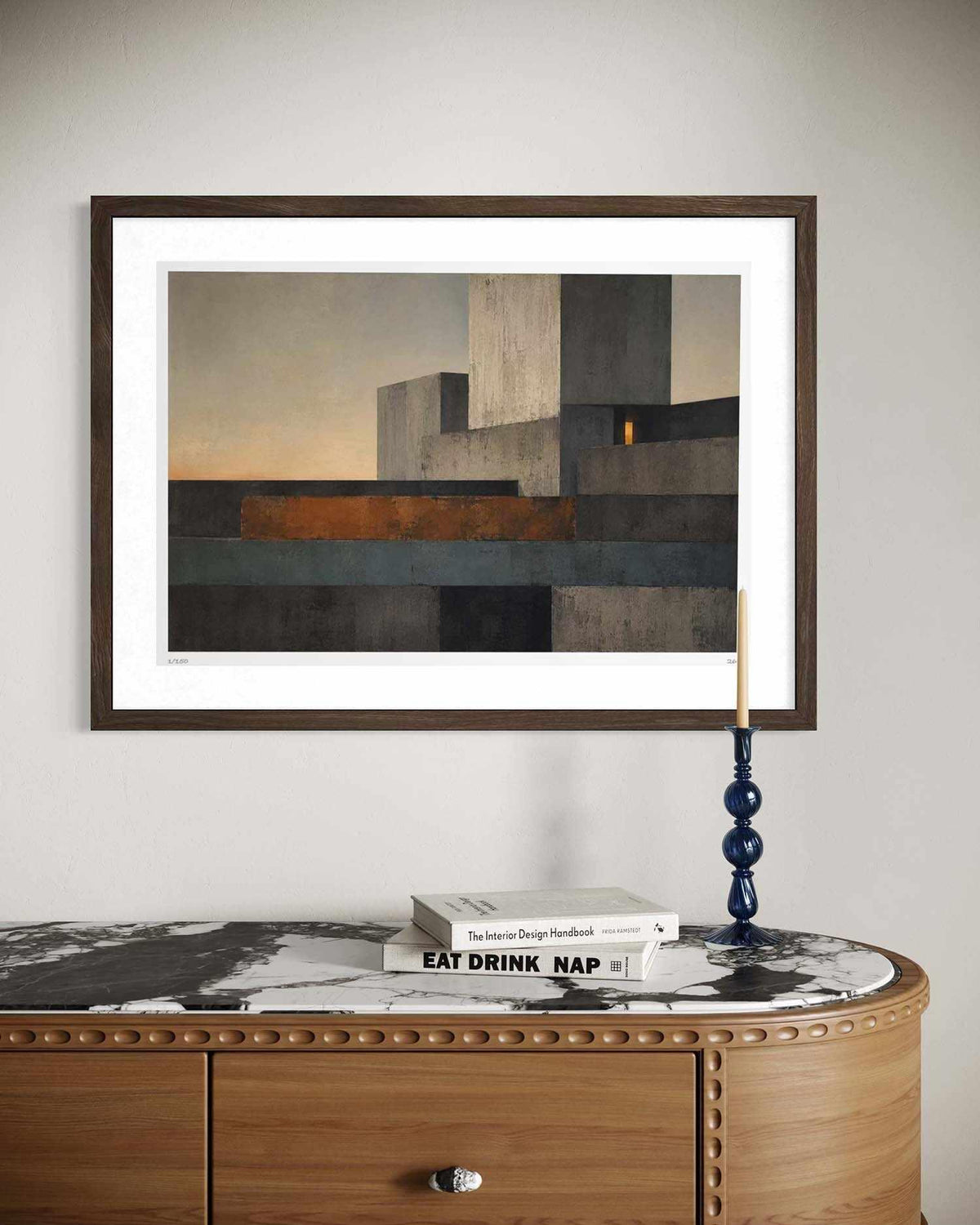 A framed abstract geometric art print with a white mat and dark wood frame, displayed on a light gray wall above a wooden console table with a marble top.