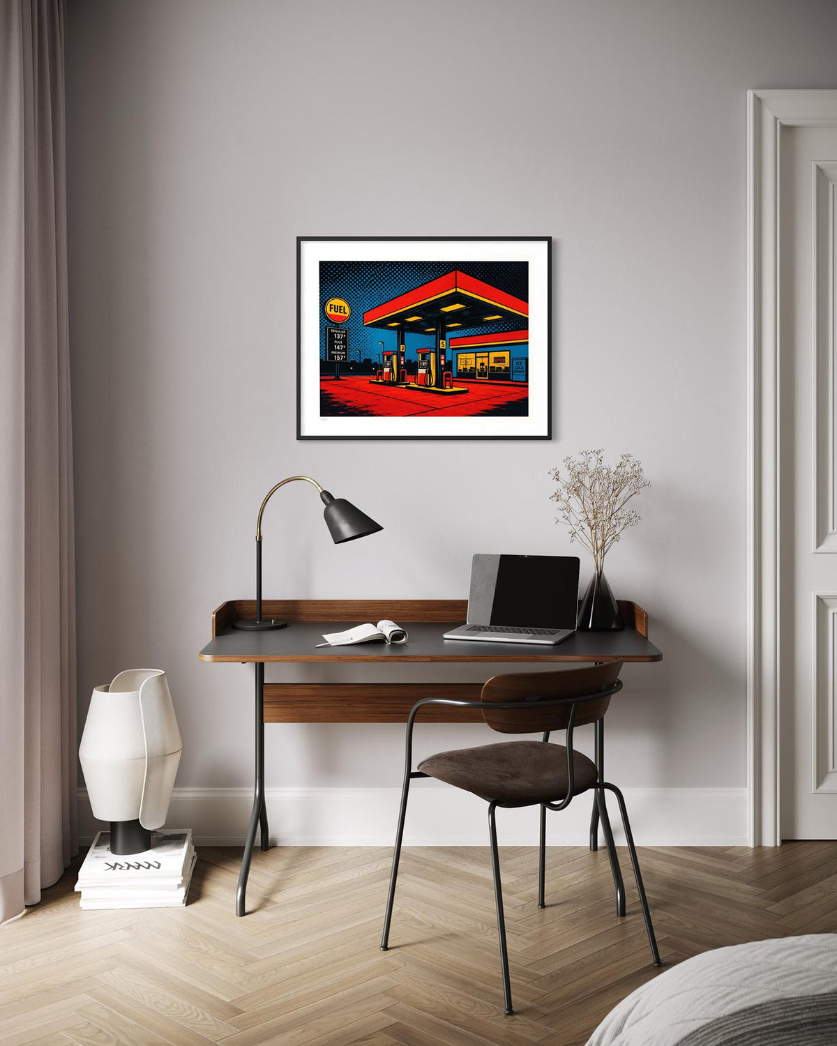 A framed art print of a vibrant, retro-style neon gas station hanging on a light gray wall above a wooden desk in a modern home office setting.