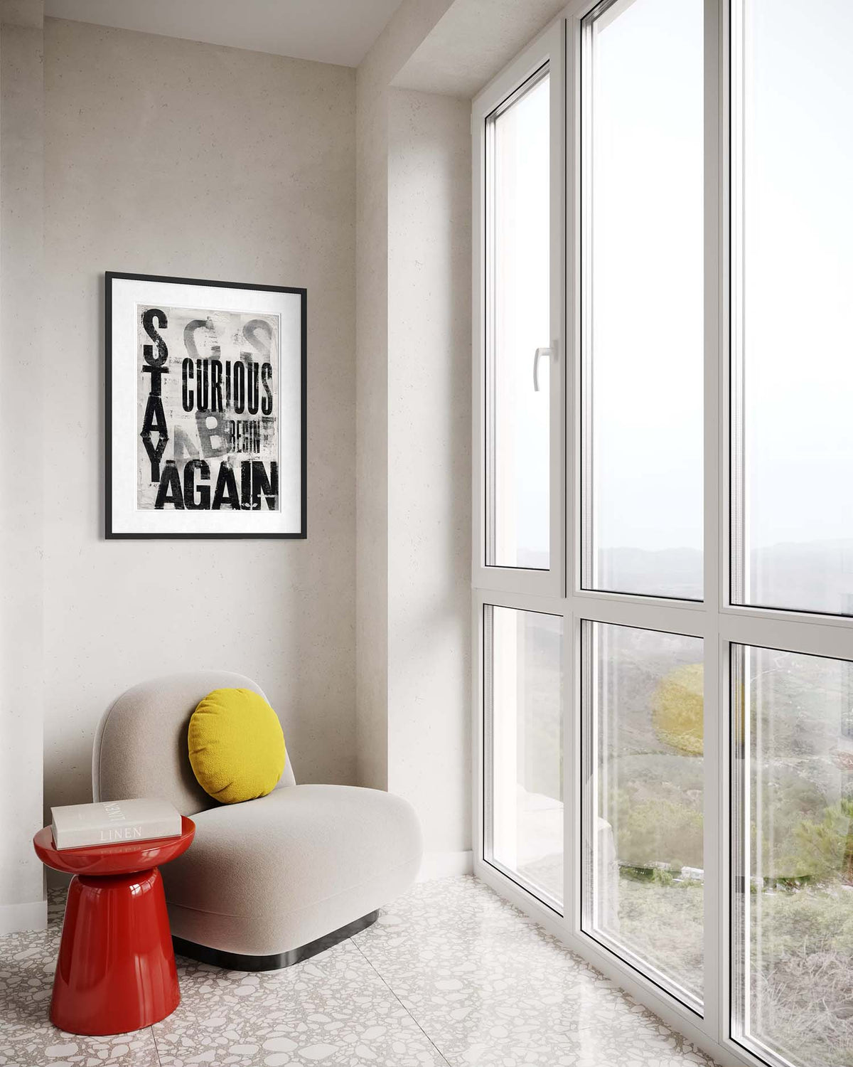 A framed black and white art print with the words 'STAY CURIOUS AGAIN' hangs on a light beige wall in a modern room. Below the print is a curved light beige armchair with a round yellow pillow, next to a small glossy red side table.