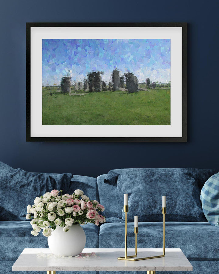 Framed artwork of Stonehenge on a blue wall above a sofa with a floral arrangement and candles.