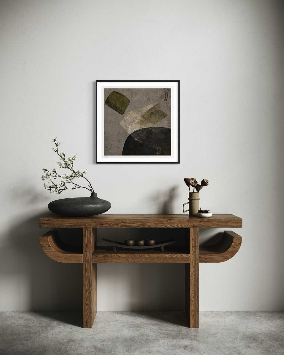 A framed abstract art print with a black frame and white mat hangs on a light gray wall above a rustic wooden console table. The print features geometric shapes in muted olive green, beige, and dark charcoal.