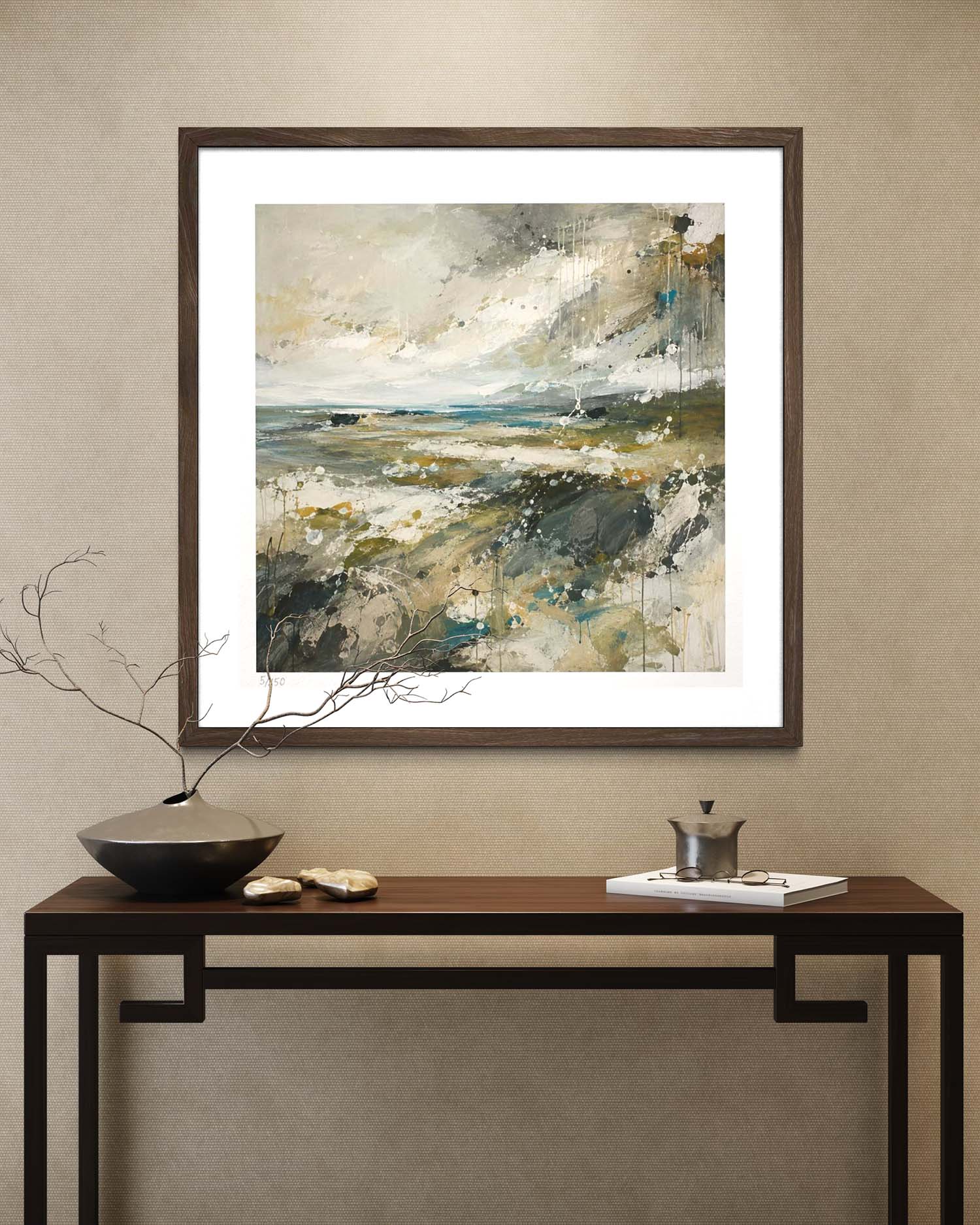 A framed abstract landscape painting hangs on a beige wall above a dark wood console table with decorative objects.
