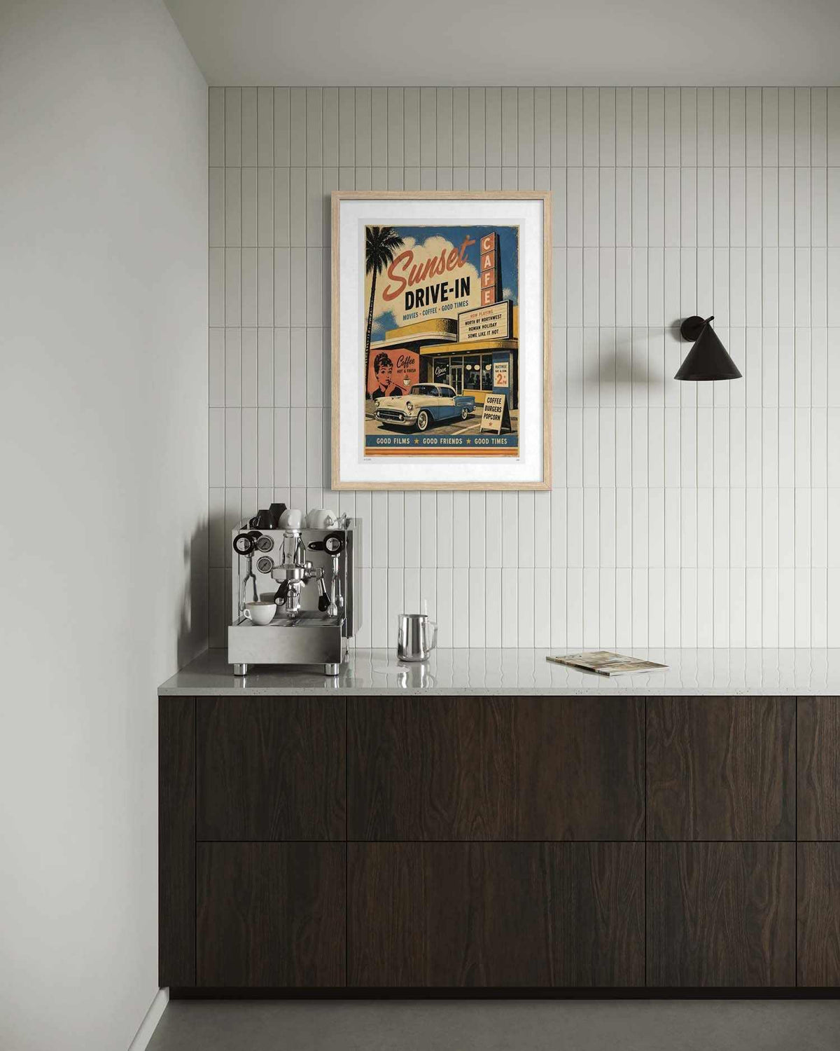 A framed vintage-style movie poster hangs on a white tiled wall above a dark wood counter with a stainless steel espresso machine and glassware in a modern interior setting.