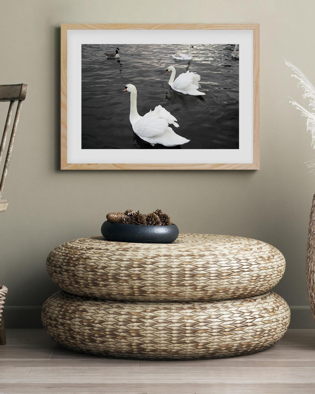 Framed artwork of swans on a wall above a woven ottoman.