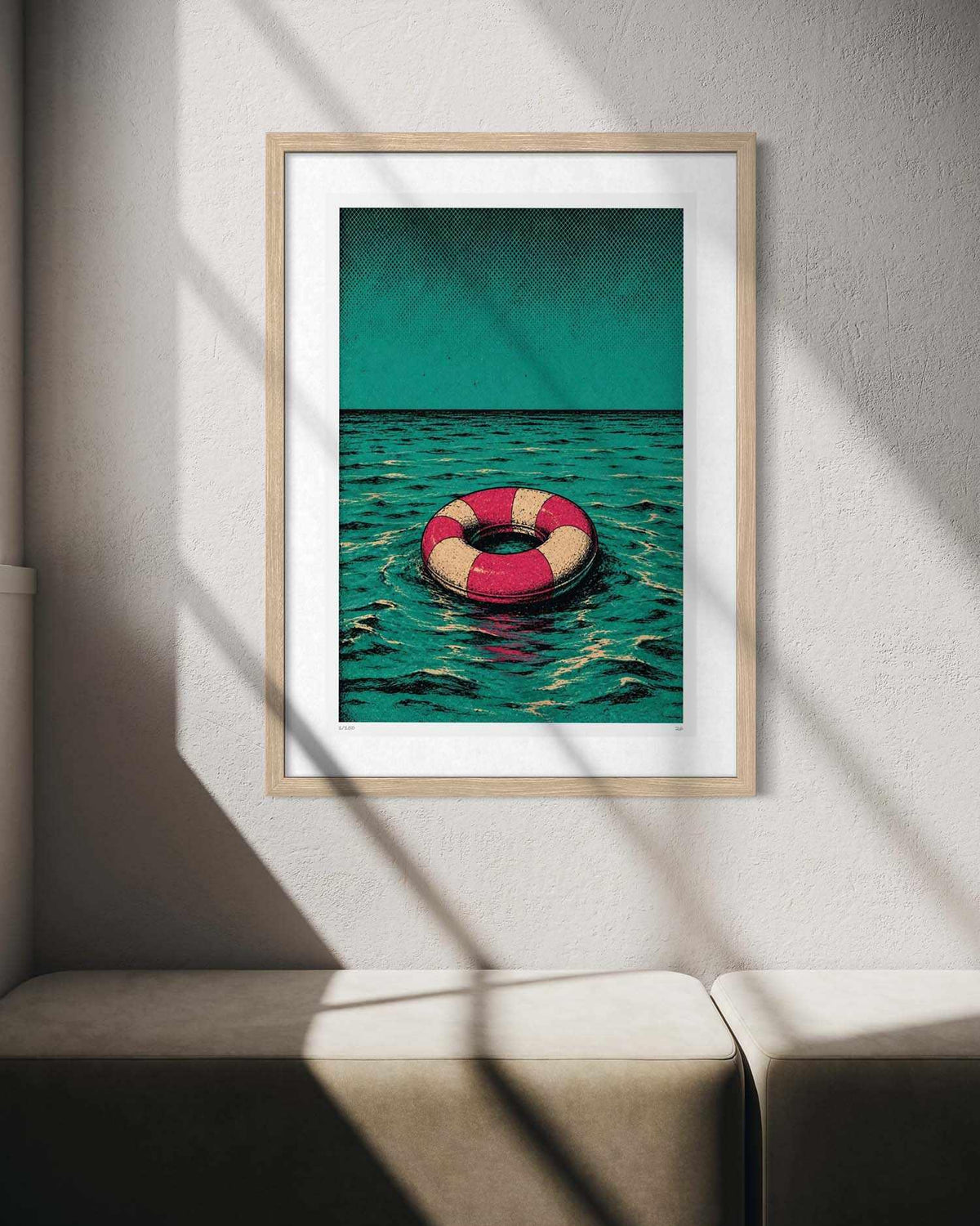 A framed art print featuring a red and cream life preserver floating on teal water under a teal sky, displayed on a textured light gray wall with diagonal window shadows.