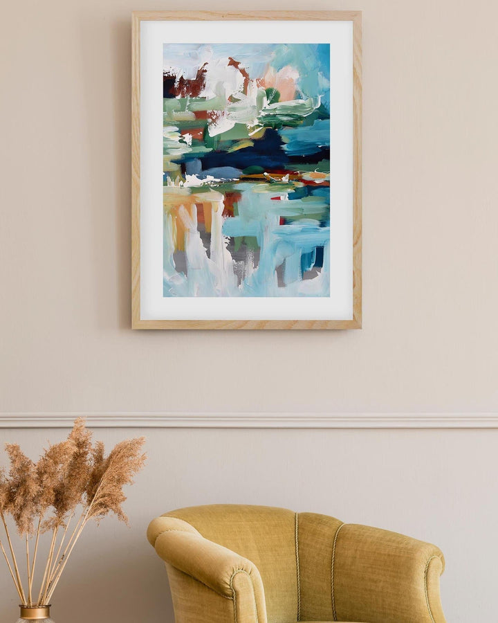 Framed abstract painting on a wall above a yellow armchair with decorative elements.