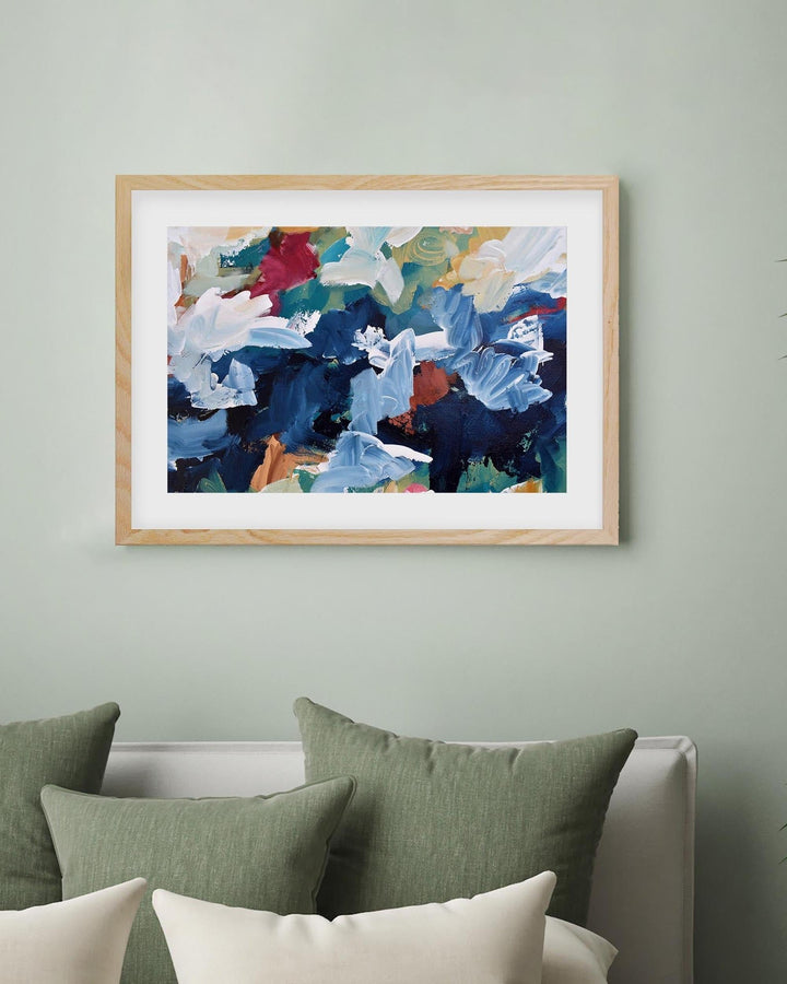 Framed abstract art on a wall with green and white pillows below.