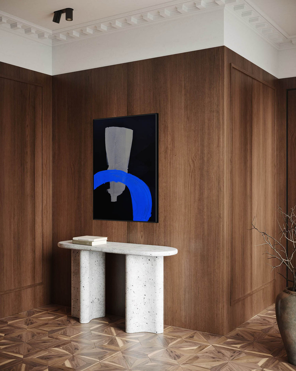 A framed abstract wall art print with a black background, gray geometric shape, and bold blue arc, displayed on a dark wood-paneled wall above a white stone console table in a modern interior.