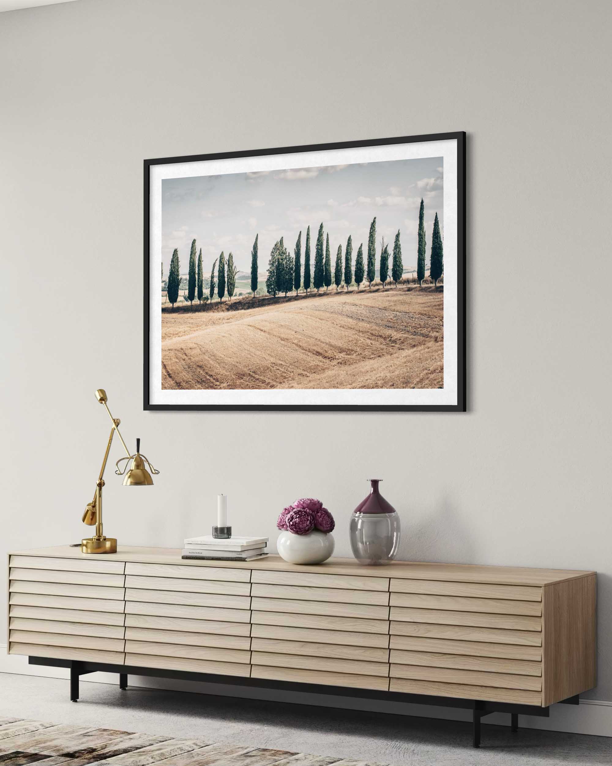 Framed landscape print on a wall above a wooden sideboard with decorative items.