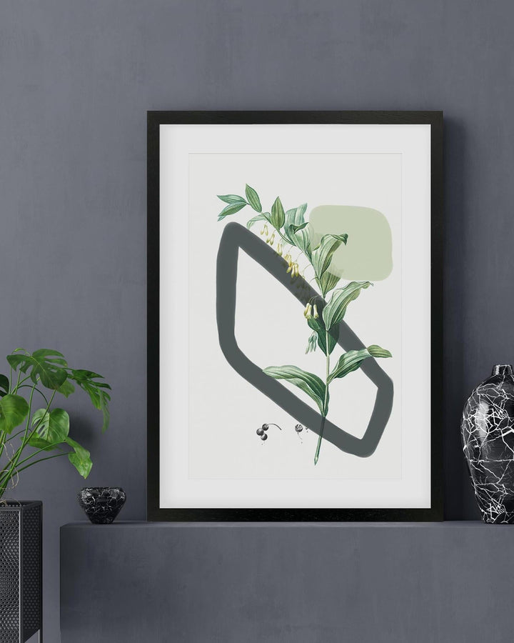 Framed artwork with green leaves and a black abstract shape on a white background, displayed on a dark gray wall.