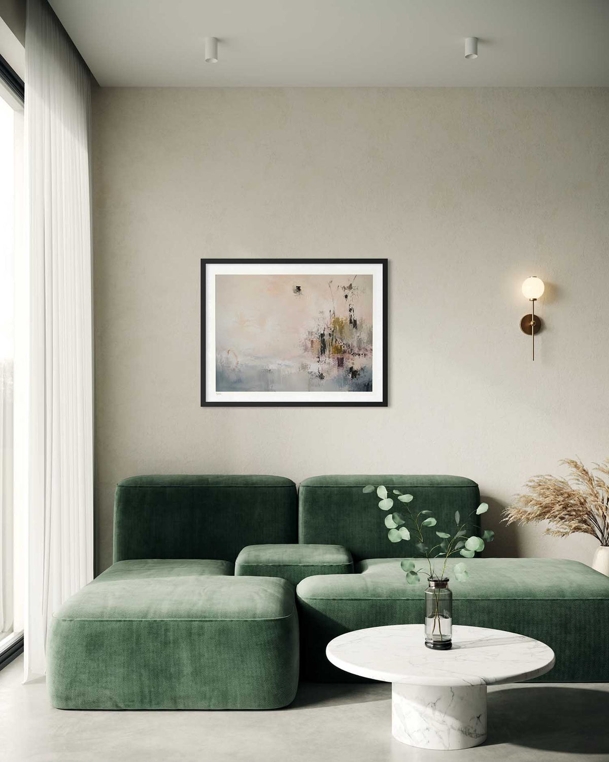 A framed abstract art print with soft pink, beige, and gray tones hangs on a textured beige wall above a modern dark green sectional sofa in a minimalist living room setting.