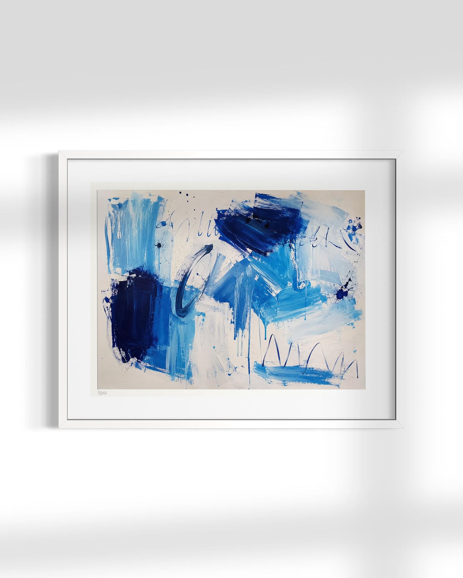 An abstract art print featuring blue and navy brushstrokes on a cream background, presented in a white frame against a light gray wall.