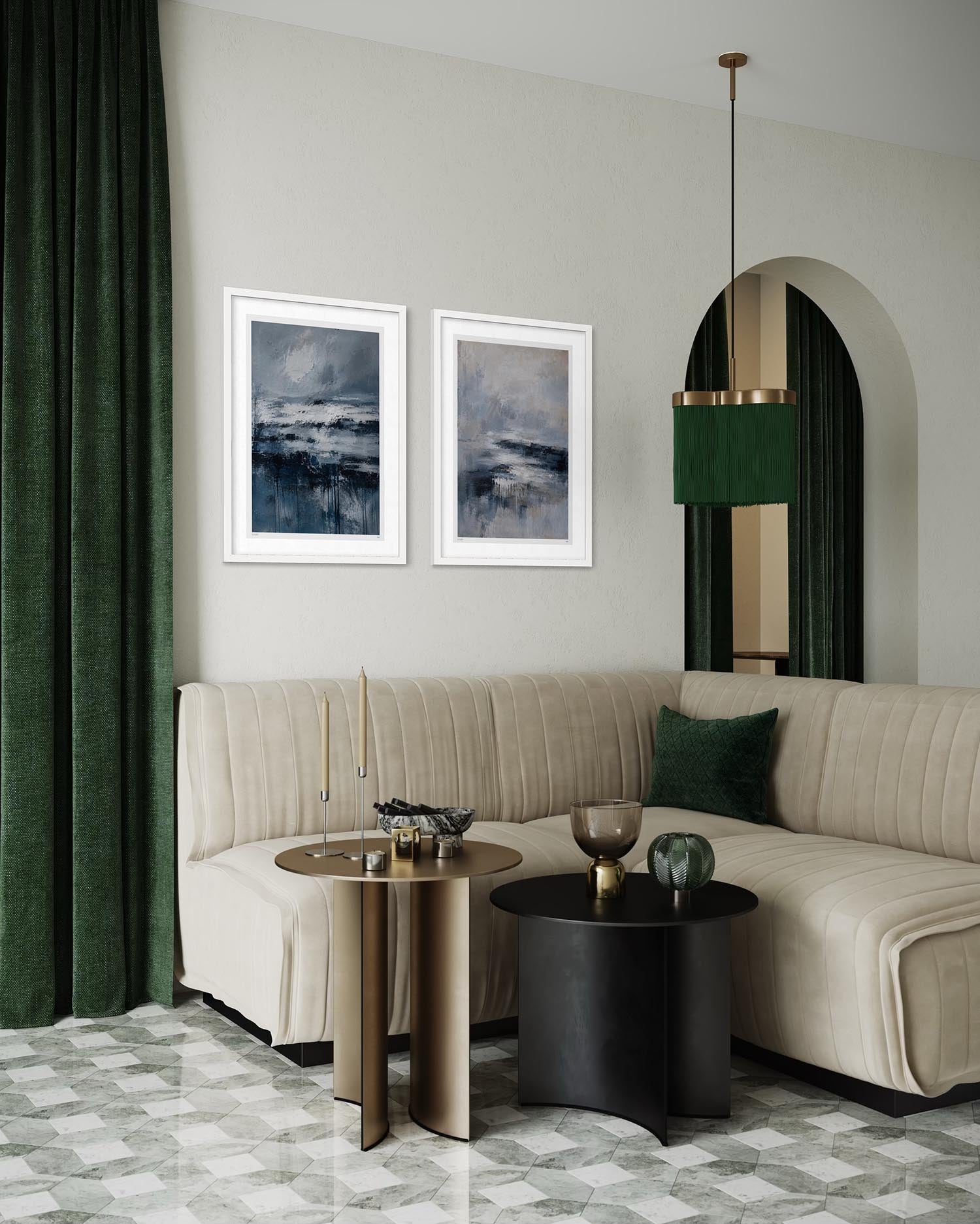 A styled living room featuring a beige sectional sofa, two dark green velvet curtains, and two framed abstract landscape prints on a light gray wall.