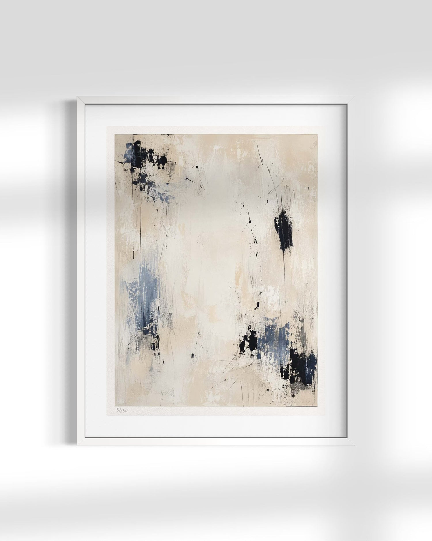 A framed abstract art print featuring a textured beige background with blue and black paint splatters, presented in a white frame against a light gray wall.