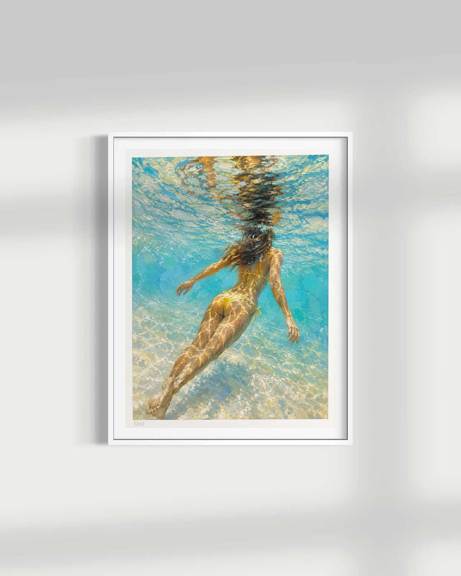 A framed art print featuring an underwater photograph of a woman swimming in turquoise blue water, displayed on a light gray wall with soft shadows.
