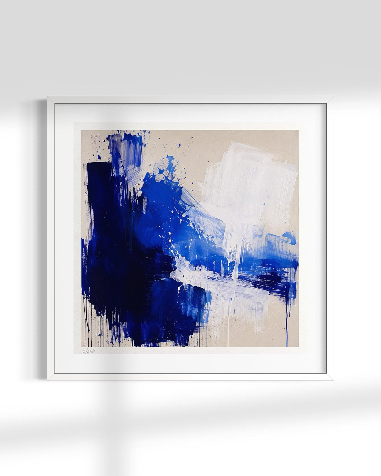 Framed abstract wall art featuring bold blue and white paint strokes on a warm beige background, presented in a white frame against a light gray wall.