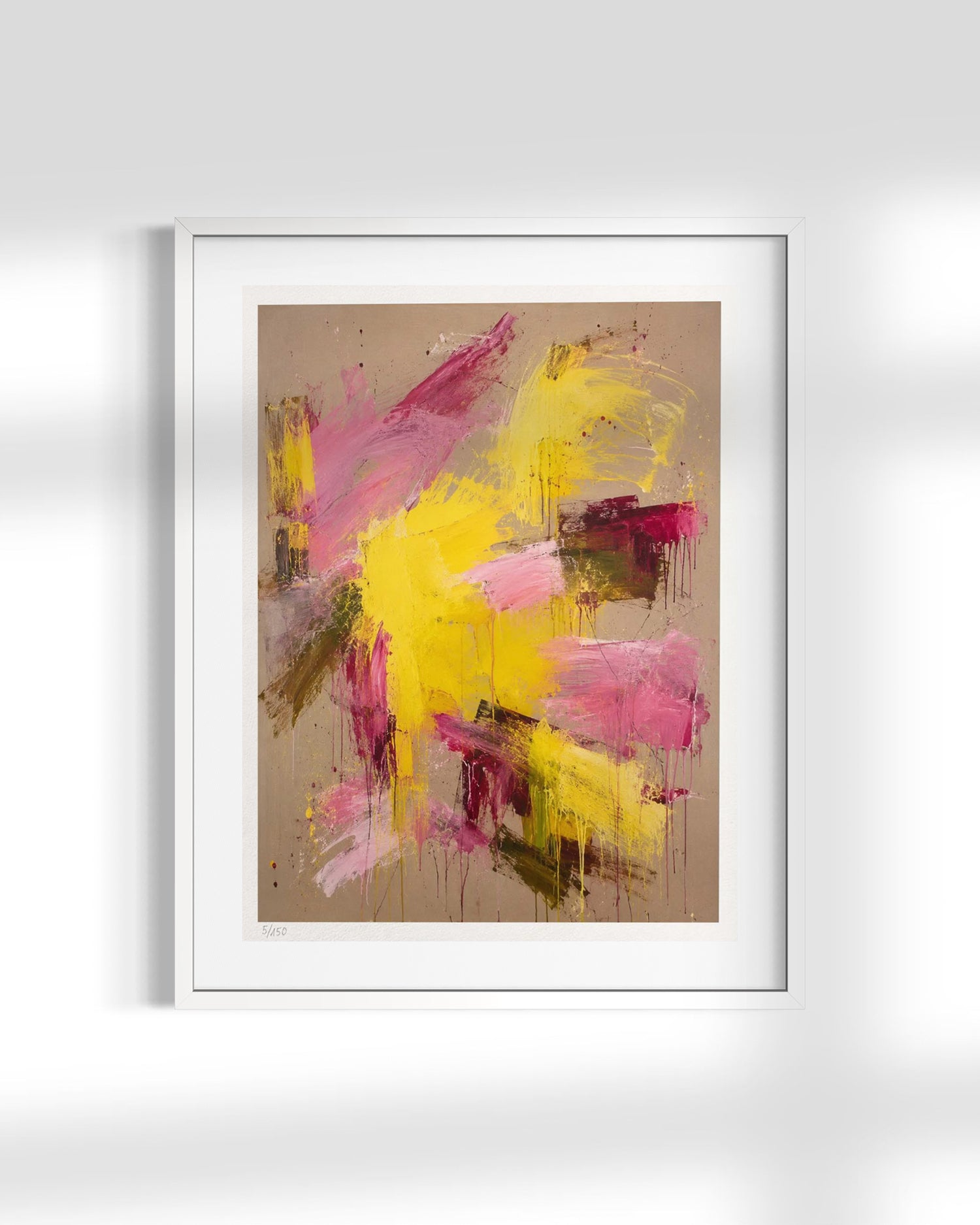 A framed abstract art print featuring expressive brushstrokes in yellow, pink, and magenta on a warm beige background, presented in a white frame against a light gray wall.