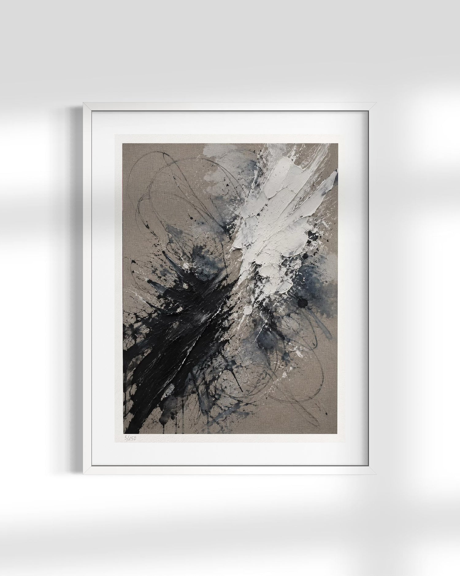 A framed abstract art print featuring black, white, and gray paint splatters on a textured beige background, presented in a white frame against a light gray wall.