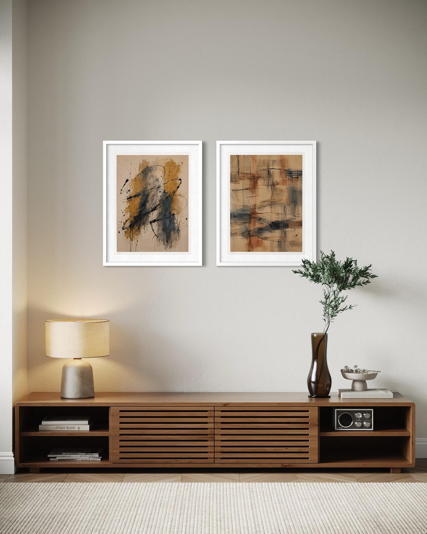 Two framed abstract art prints with white frames hang on a light gray wall above a wooden media console in a styled living room setting.