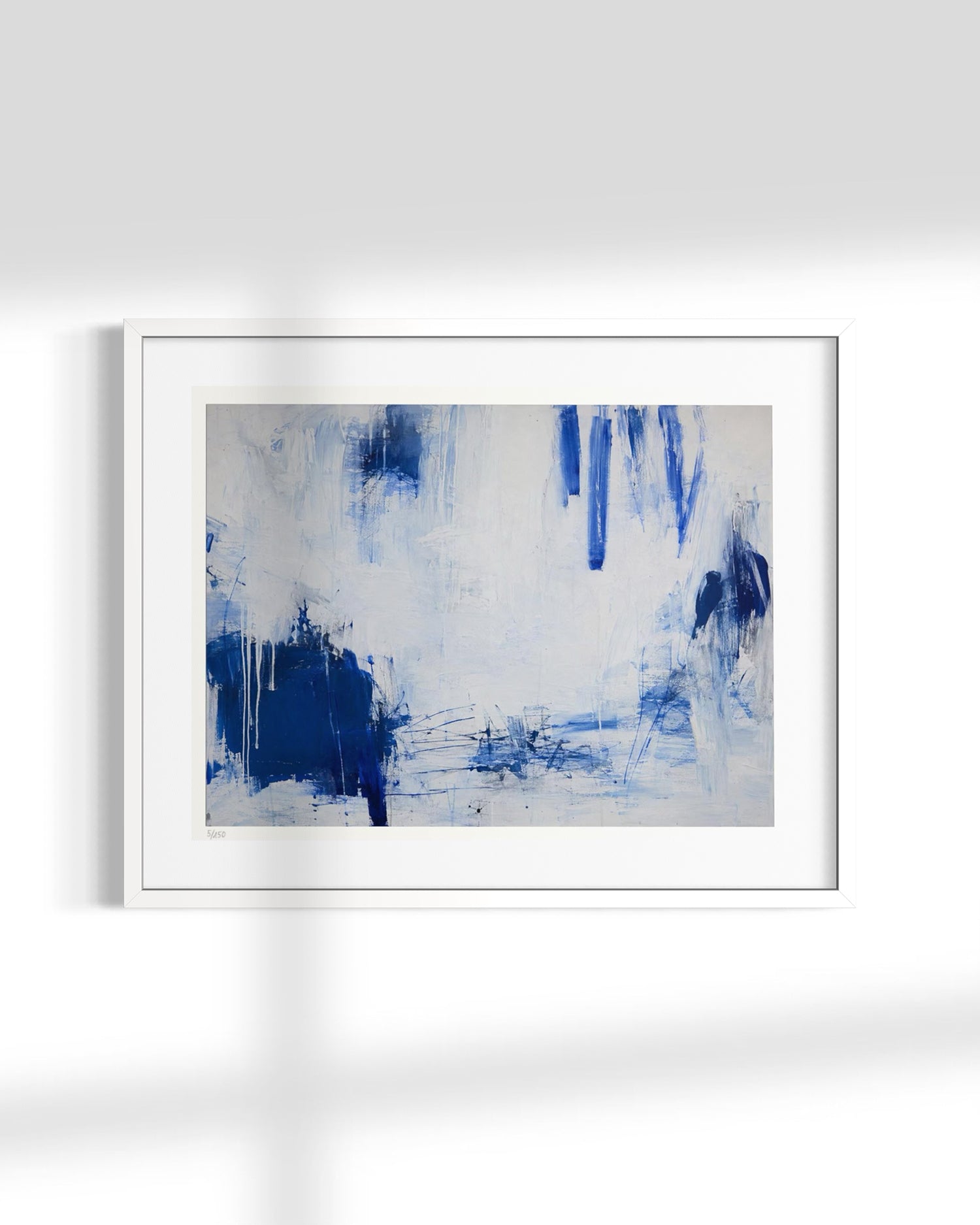 A framed abstract art print featuring blue and white brushstrokes, displayed on a clean white wall with soft window shadow overlays.