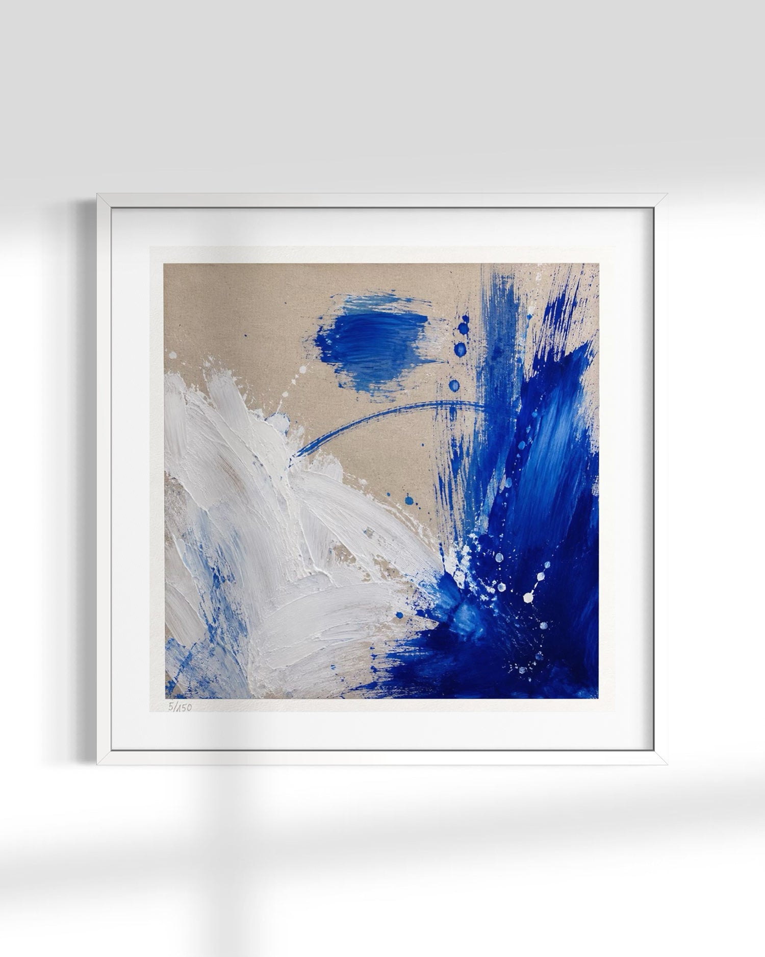 Framed abstract wall art featuring bold blue and white paint strokes on a warm beige background, presented in a white frame against a light gray wall.