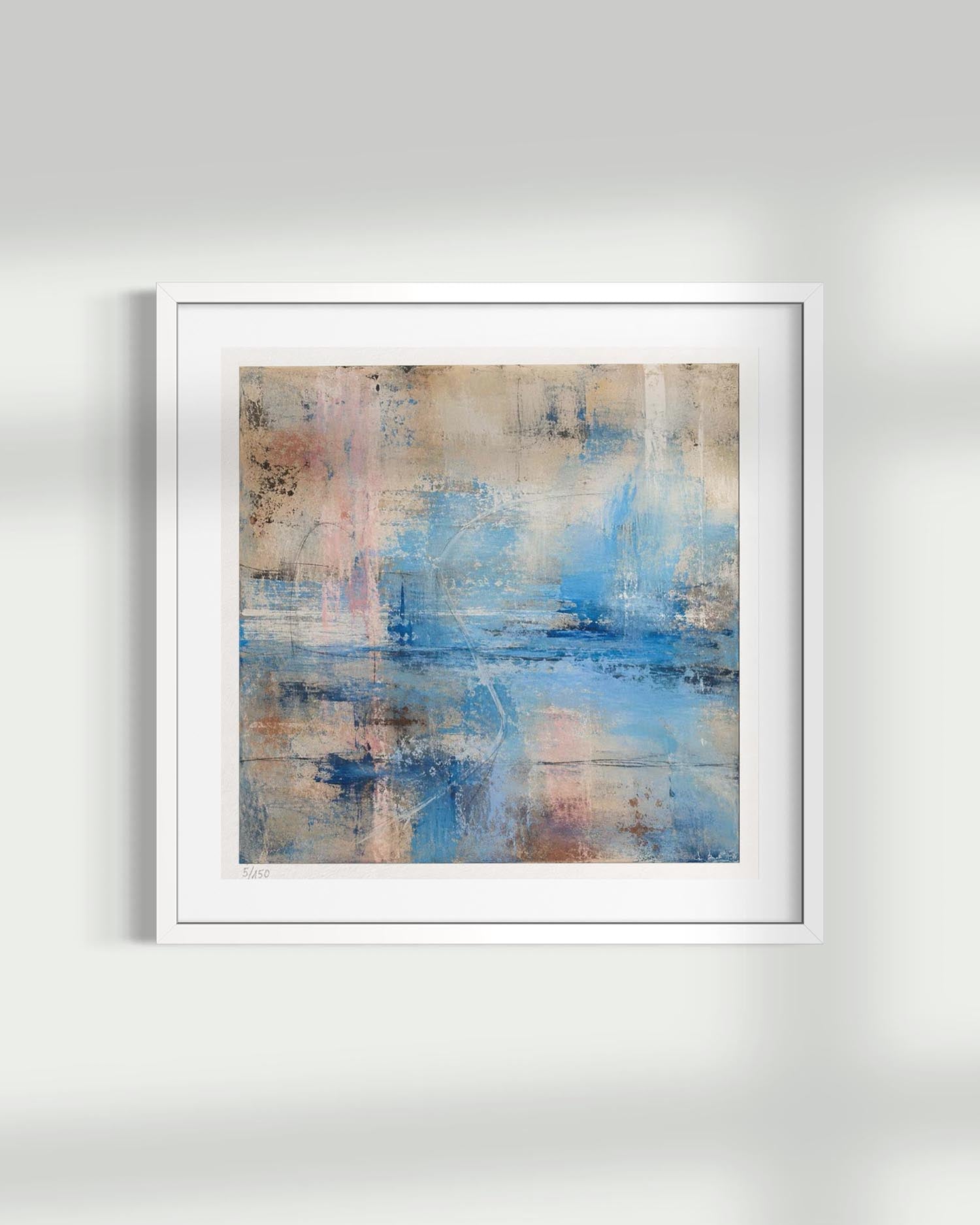 Framed abstract wall art hanging on a light gray wall, featuring a white frame with a square canvas showing blended blue, beige, and soft pink brushstrokes.